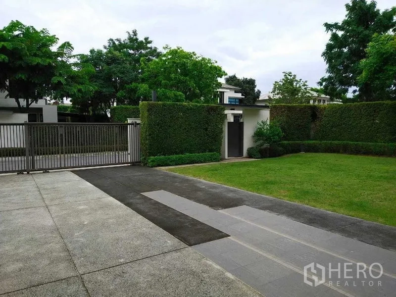 独立式住宅 出租或出售在Mueang Nonthaburi, Nonthaburi - 带金属大门的车道，绿篱环绕与宽阔前庭草地。