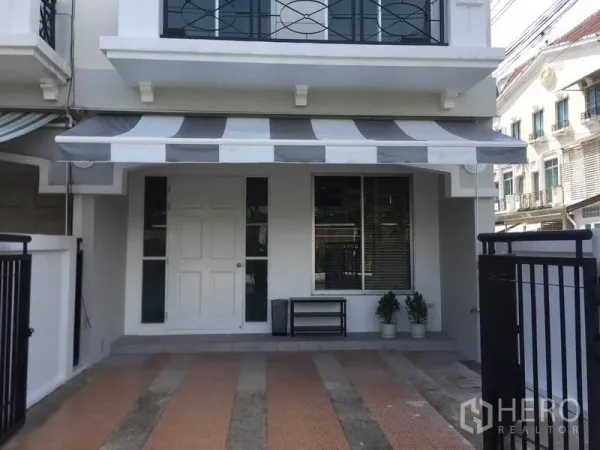 ทาวน์เฮาส์ ให้เช่าในLat Phrao, Bangkok - หน้าบ้านมีกันสาดลายทาง ประตูสีขาว หน้าต่างบานใหญ่ และพื้นกระเบื้องที่จอดรถ