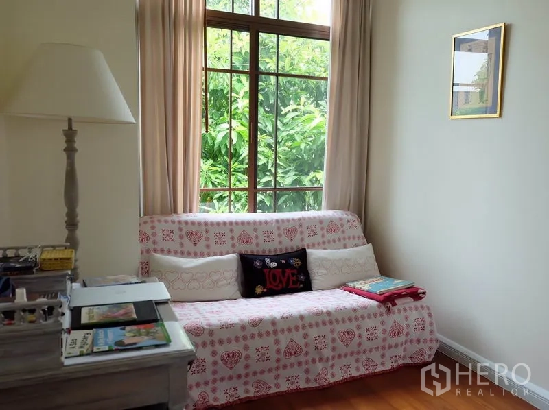 Detached House for rent in Watthana, Bangkok - Cozy reading nook with a patterned sofa beside a tall window overlooking lush greenery.