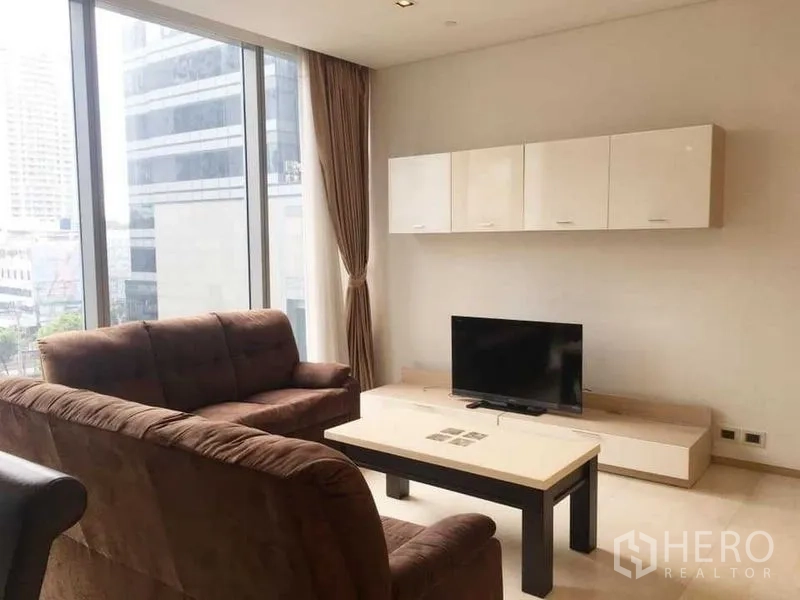 Condominium for rent in Bang Rak, Bangkok - Bright lounge with TV unit, wall cabinets, and floor-to-ceiling windows with curtains.