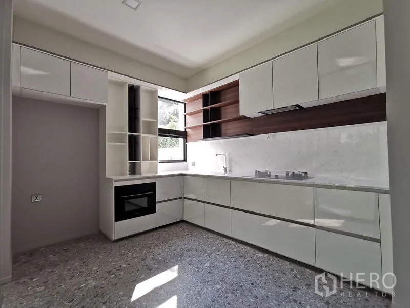 Detached House for sale in Saphan Sung, Bangkok - Separate L-shaped kitchen with glossy cabinetry, window and stone flooring.