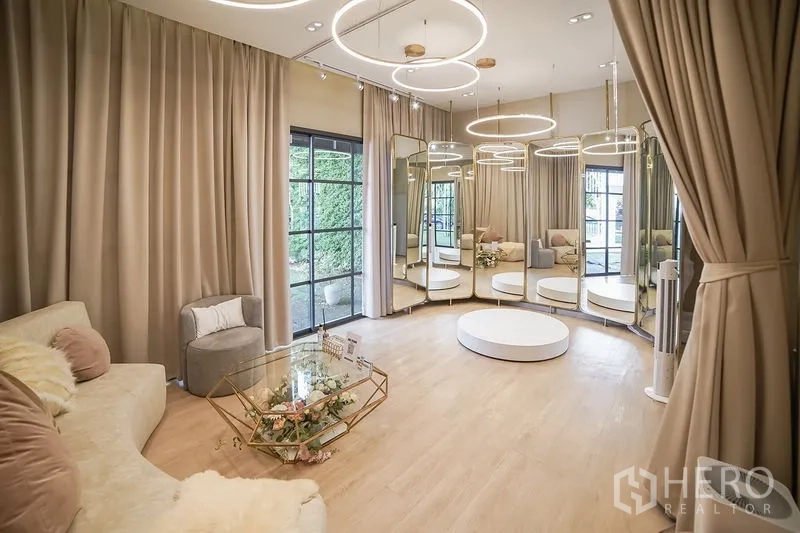 Detached House for rent in Huai Khwang, Bangkok - Elegant studio-style living room with circular ring lights, wall mirrors and light wood flooring.