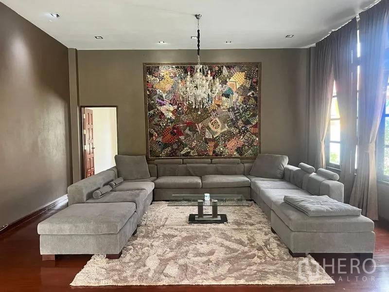 Detached House for sale in Prawet, Bangkok - Spacious lounge with U-shaped grey sectional, chandelier, and large wall art.