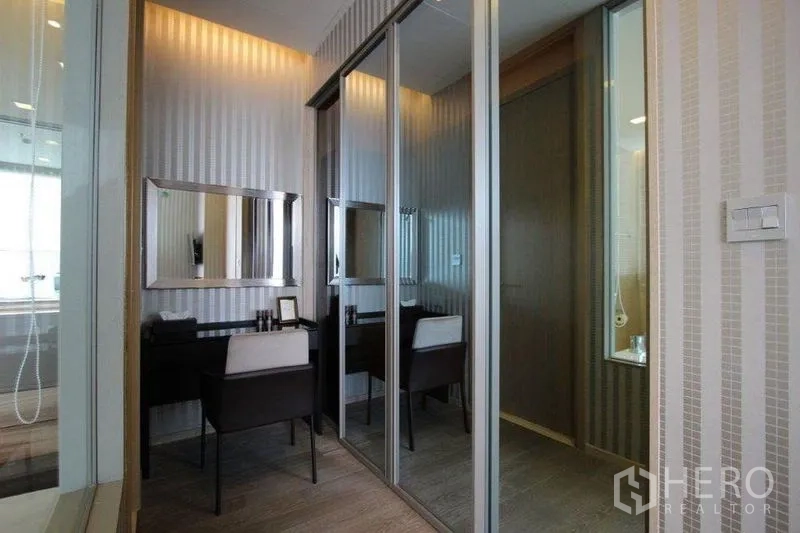 Condominium for rent in Watthana, Bangkok - Bedroom dressing area with mirrored wardrobes and a work vanity against striped wallpaper.