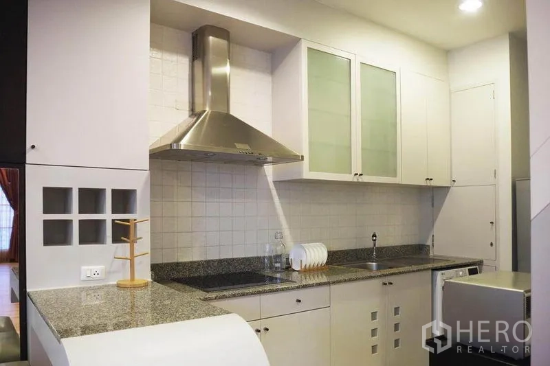 Condominium for rent in Khlong Toei, Bangkok - Fitted kitchen with granite countertops, stainless hood, tiled backsplash, and upper cabinets.