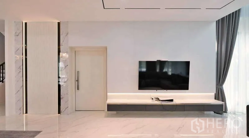 Detached House for rent or sale in Thanyaburi, Pathum Thani - Bright living room with marble-look flooring, wall-mounted TV unit and full-height curtains.
