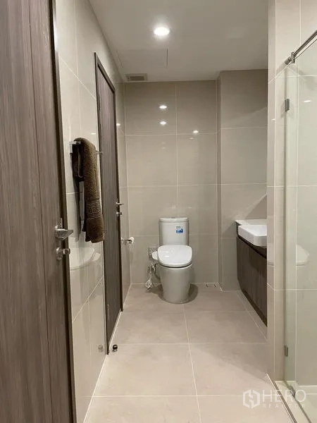 公寓 出租在Bang Na, Bangkok - 宽敞浴室走廊，坐便器、玻璃淋浴房与木纹门。