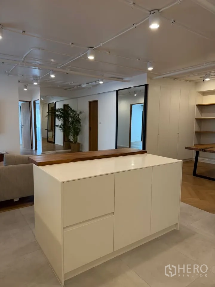 Condominium for rent in Watthana, Bangkok - Open-plan area with white island cabinet, track lights, and potted plants.