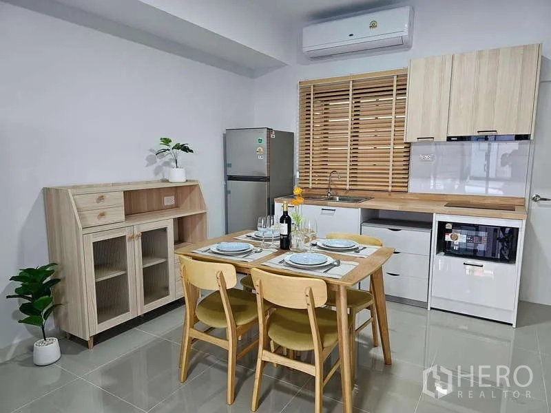 Townhouse for rent in Bang Phli, Samut Prakan - Fitted kitchen with wooden cabinets, dining set, fridge, microwave and air conditioner.