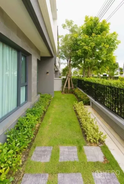 Detached House for rent or sale in Bang Phli, Samut Prakan - Side garden with trimmed lawn, stepping-stone path, hedges and mature trees beside the house.