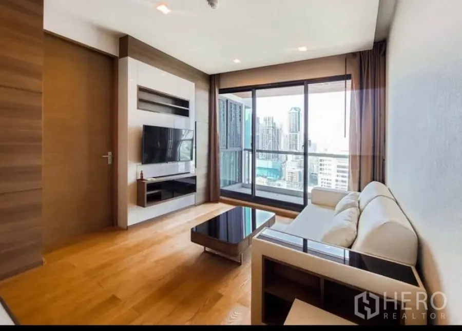 公寓 出租在Bang Rak, Bangkok - 客厅明亮，配沙发与电视墙，落地窗通向带城景的阳台