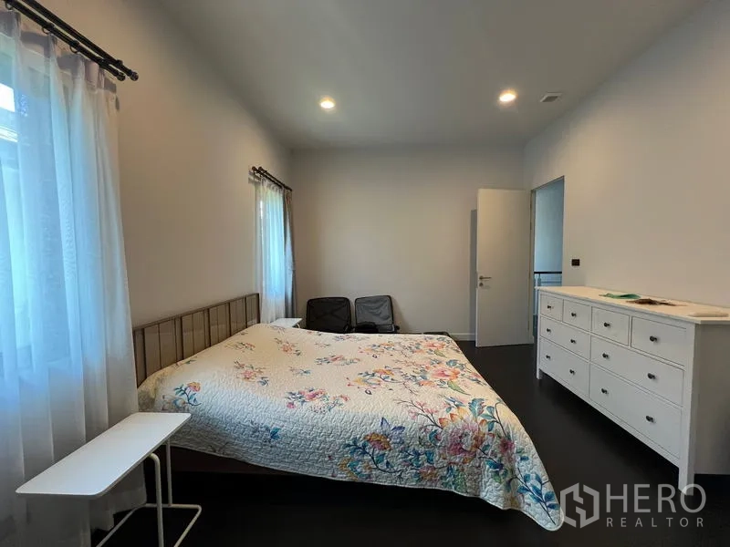 Detached House for rent in Bang Kapi, Bangkok - Guest bedroom with floral bedding, white dresser and dark flooring.