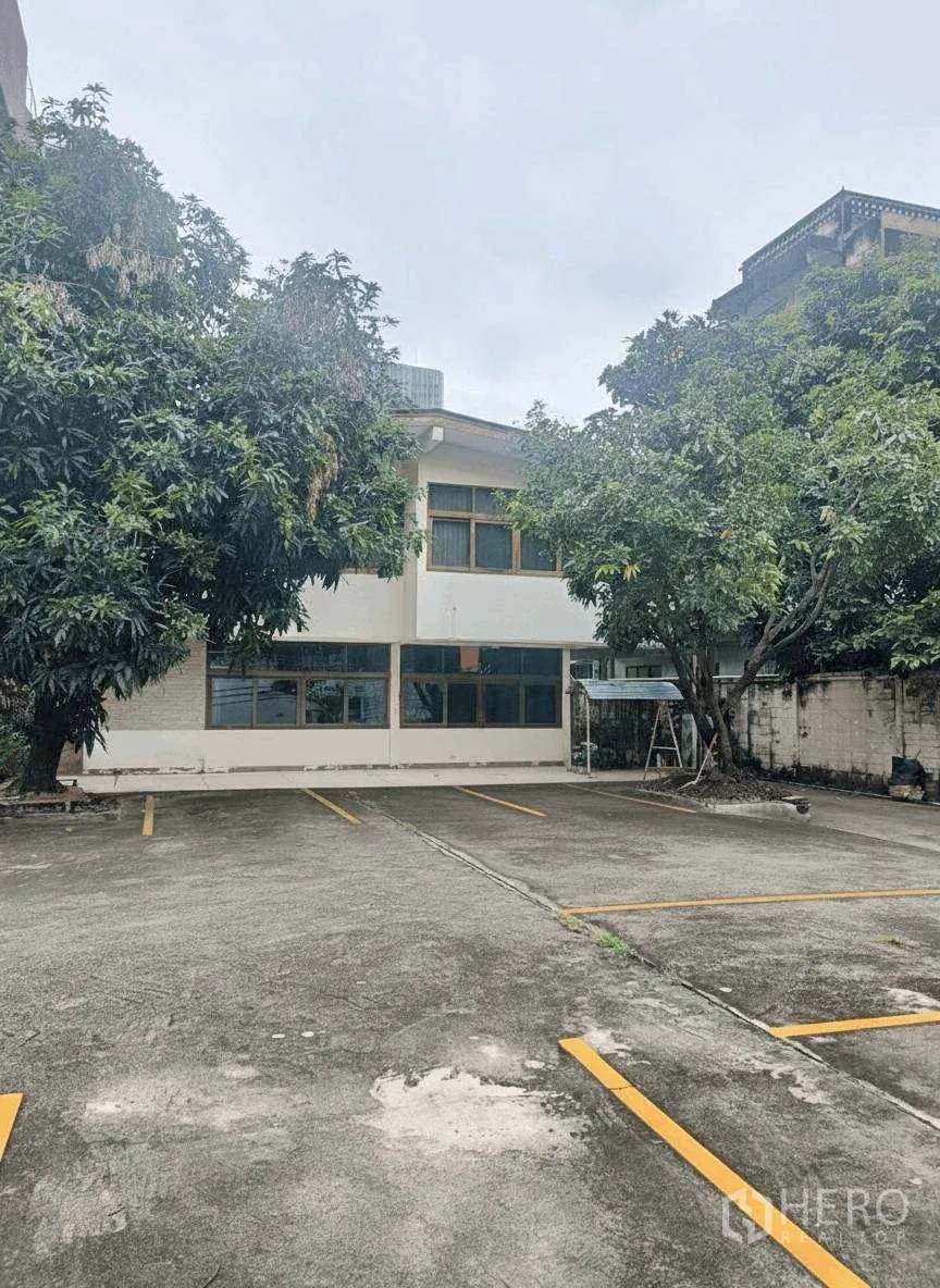 Home Office for rent in Bang Rak, Bangkok - Exterior of a two-storey building with tree-shaded parking spaces.