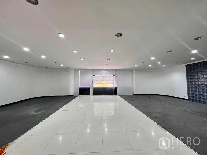 Shophouse for rent in Khlong San, Bangkok - Wide showroom area with recessed spotlights, glossy tile walkway and a glass front.
