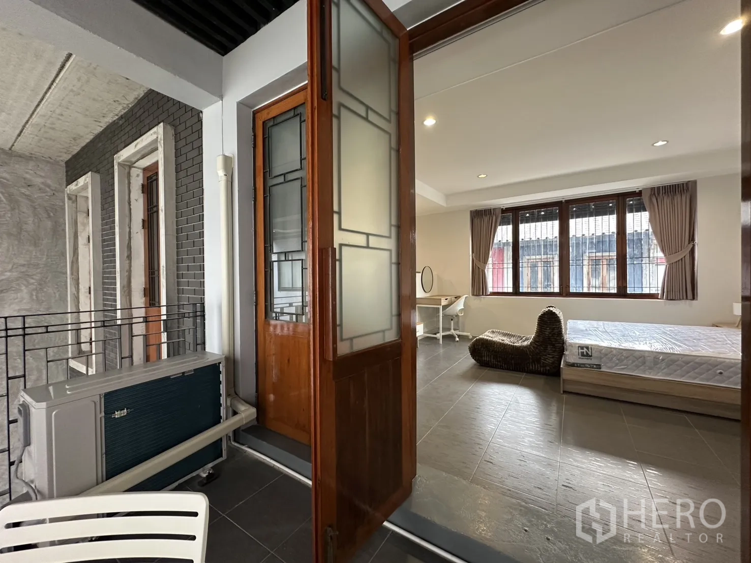 Apartment for rent in Pathum Wan, Bangkok - Bedroom with work desk and doors to a covered terrace with a round table.