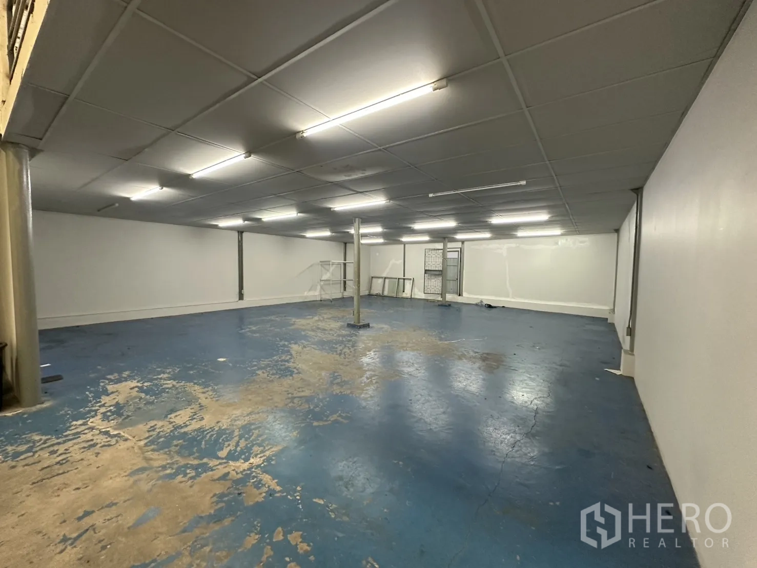 Warehouse for rent in Suan Luang, Bangkok - Wide storage hall with blue floor and metal shelving units.