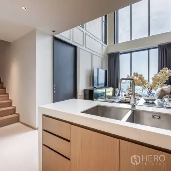 คอนโด ให้เช่าในKhlong Toei, Bangkok - ครัวแบบเปิดมีซิงก์บนไอส์แลนด์ ตู้ไม้ มองออกไปยังห้องนั่งเล่นและผนังกระจก สูง ใกล้บันได