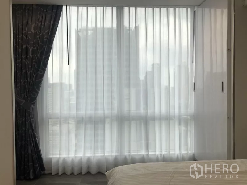 公寓 出租在Sathon, Bangkok - 卧室转角落地窗，纱帘与部分城市天际线景观。