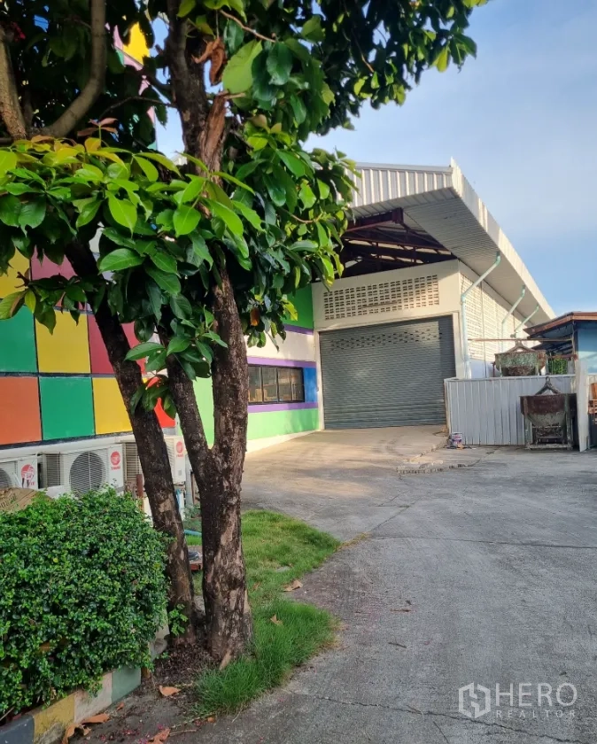 คลังสินค้า for sale in Bang Bon, Bangkok - หน้าทางเข้าโกดังมีประตูม้วนไฟฟ้า ข้างสวนหย่อม