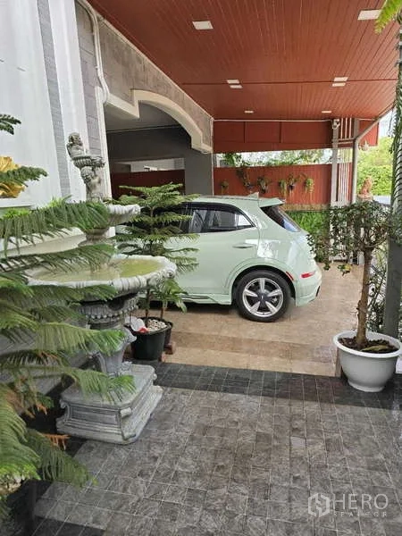 Detached House for rent in Thanyaburi, Pathum Thani - Covered carport with tiled floor, red ceiling panels and potted plants at the front of the single house.