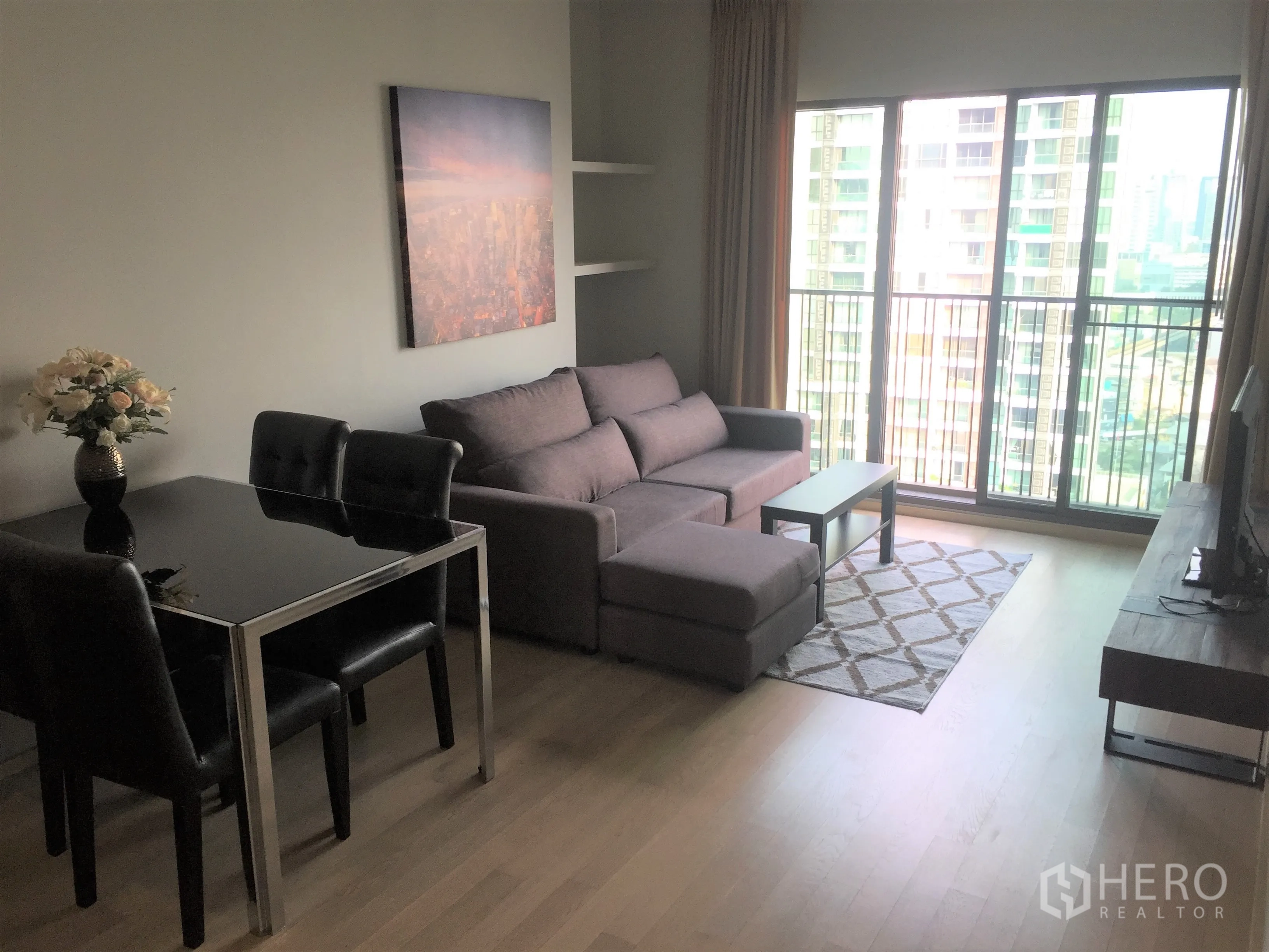 คอนโด ให้เช่าในBangkok - ห้องนั่งเล่นสว่างพร้อมหน้าต่างสูงเต็มบาน ระเบียงชมวิวเมือง โซฟา พรม และชั้นวางทีวี