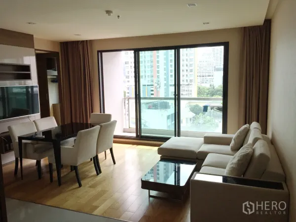 公寓 出租在Bang Rak, Bangkok - 开放式客餐厅，L形沙发与四人餐桌，连通可观城市景的阳台。