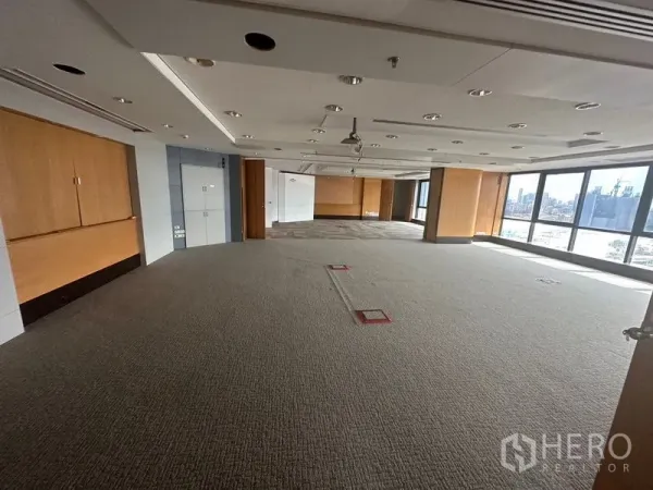 Office Space for rent in Khlong Toei, Bangkok - Expansive office floor with carpet, wall panels, and panoramic windows flooding the space with light.