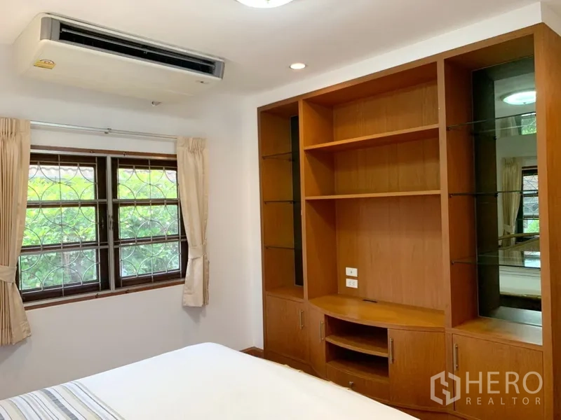 Detached House for rent in Khlong Toei, Bangkok - Bedroom with built-in wooden shelving, air-conditioning and garden-view window.