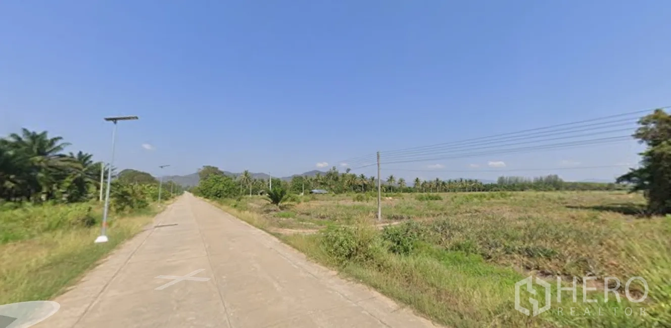 Land for sale in Mueang Prachuap Khiri Khan, Prachuap Khiri Khan - Concrete road with streetlights beside farmland and a mountain backdrop.