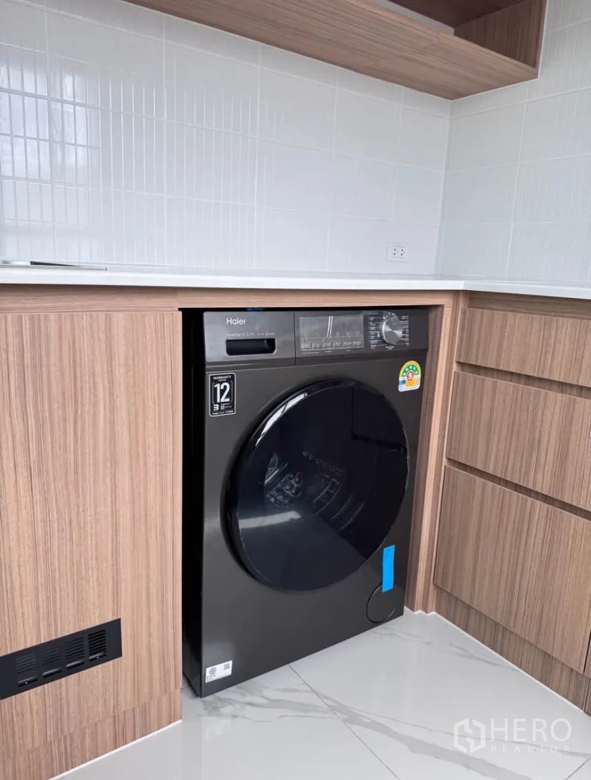 Detached House for rent in Samut Prakan - Laundry nook with built-in cabinetry and a front-load washing machine.