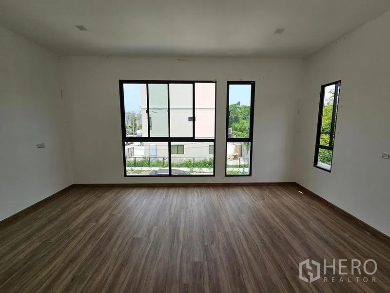 联排别墅 出租在Bang Kapi, Bangkok - 转角卧室，黑框多扇窗与木纹地板，俯瞰花园景观。