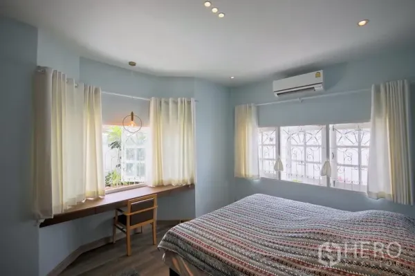 Detached House for rent in Bang Kapi, Bangkok - Airy master bedroom with bay windows, built-in wood desk, curtains, and air conditioner.