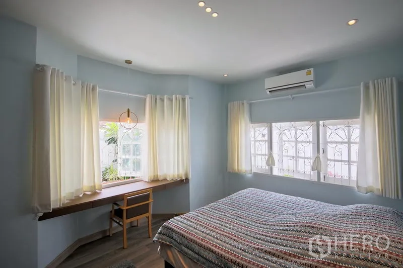 Detached House for rent in Bang Kapi, Bangkok - Airy master bedroom with bay windows, built-in wood desk, curtains, and air conditioner.