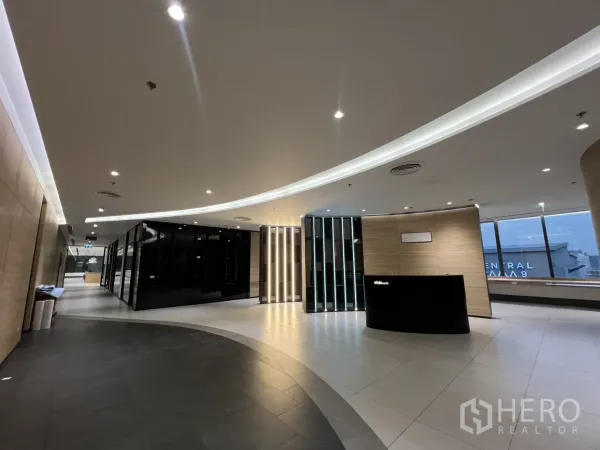 办公空间 出租在Huai Khwang, Bangkok - 弧形前台区，氛围灯光、接待台与黑色玻璃会议室，窗外城市景观。