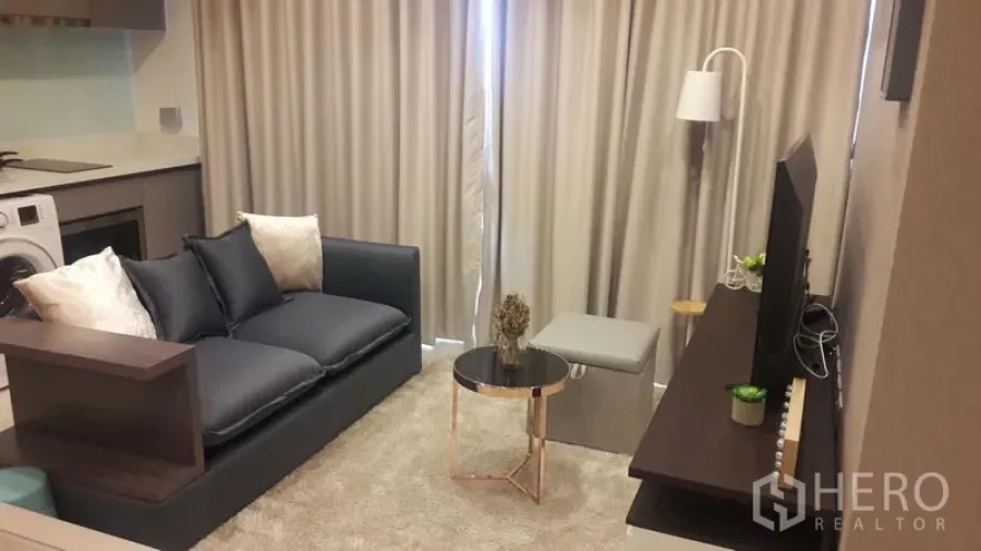 Condominium for rent in Khlong Toei, Bangkok - Cozy living room with sofa, round coffee table, floor lamp, and curtains