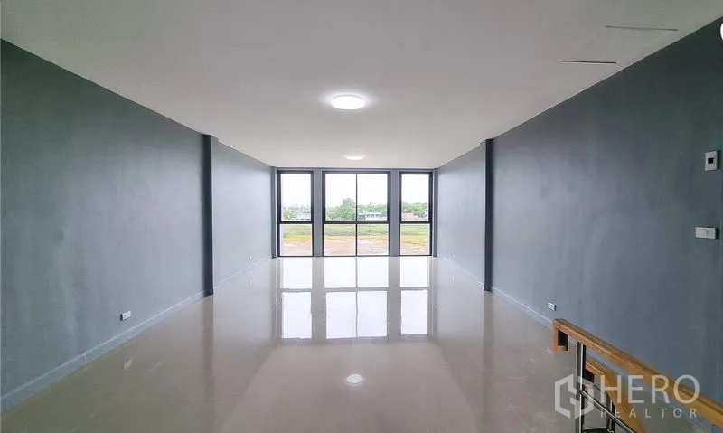 Shophouse for sale in Lam Luk Ka, Pathum Thani - Deep rectangular room with floor-to-ceiling windows at the far end.