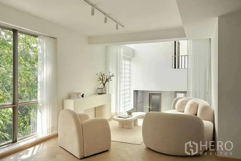 Home Office for sale in Chatuchak, Bangkok - Sunlit lounge with cream curved sofas overlooking a double‑height atrium and large window.