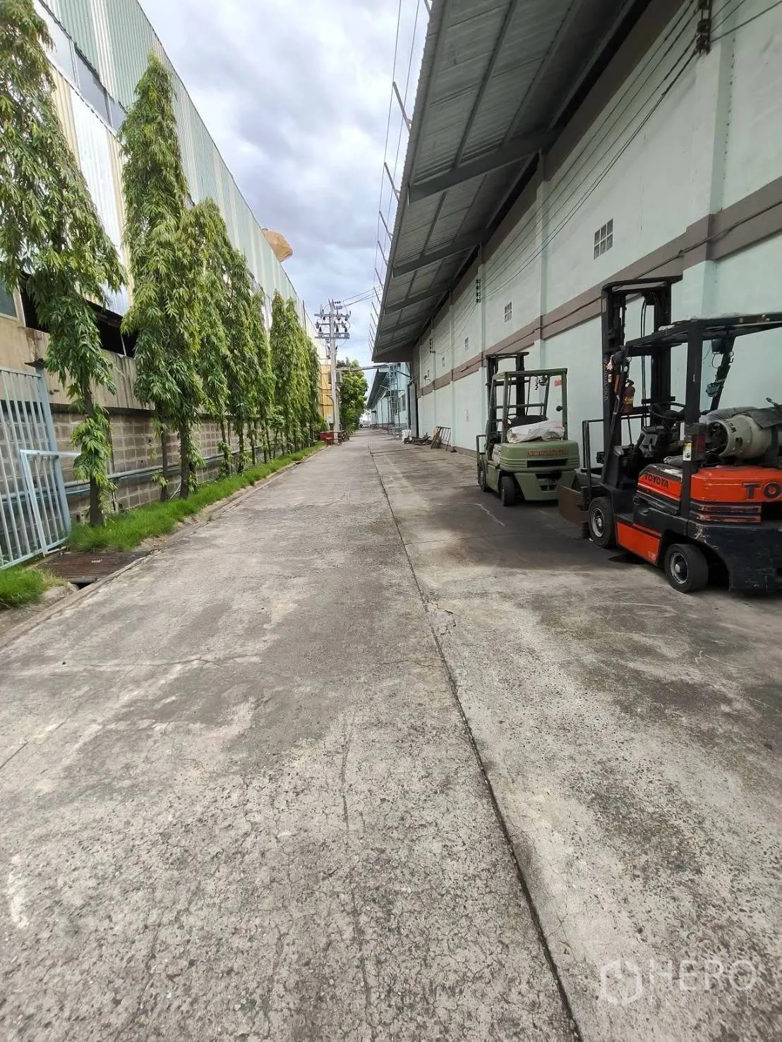 Warehouse for rent in Mueang Samut Prakan, Samut Prakan - Exterior service lane beside the warehouse with forklifts and covered eaves.