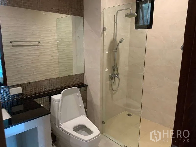 Detached House for rent - Bathroom featuring a glass-enclosed rain shower, toilet and wide mirror above dark counter.