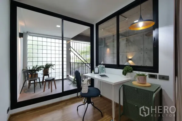 Townhouse for rent in Khlong Toei, Bangkok - Compact home office beside a glass wall opening to a balcony with glass blocks.