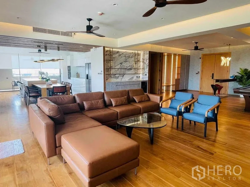 คอนโด ให้เช่าหรือขายในWatthana, Bangkok - ห้องพักผ่อนกว้างพร้อมโซฟาหนังทรงแอล เก้าอี้สีน้ำเงิน โต๊ะกระจก และผนังหินอ่อน