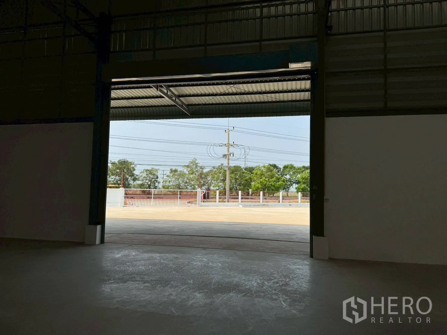 Warehouse for rent in Phutthamonthon, Nakhon Pathom - View from inside the warehouse through the roller door to the fenced yard and gate.