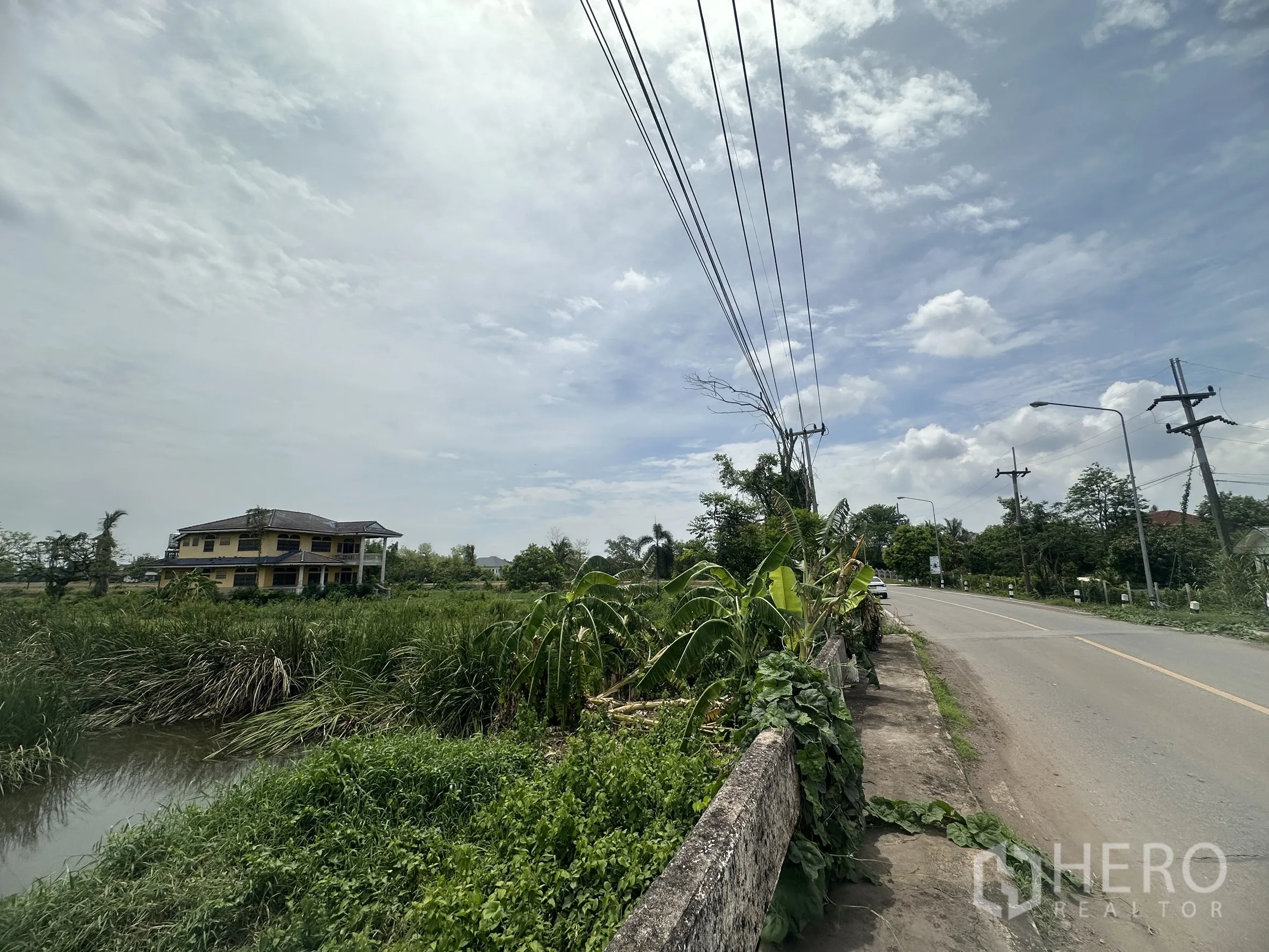 Land for sale in Bang Nam Priao, Chachoengsao - Main road with power lines running past a canal and a rural house in the distance.
