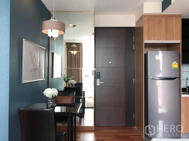 Condominium for rent or sale in Ratchathewi, Bangkok - Entry area with compact dining nook, pendant lamp, refrigerator, wood cabinetry, and dark main door.