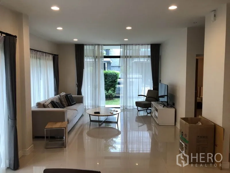 บ้าน ให้เช่าในBang Kapi, Bangkok - ห้องนั่งเล่นสว่าง โปร่งด้วยหน้าต่างสูง จัดโซฟาและทีวี มองออกสวน