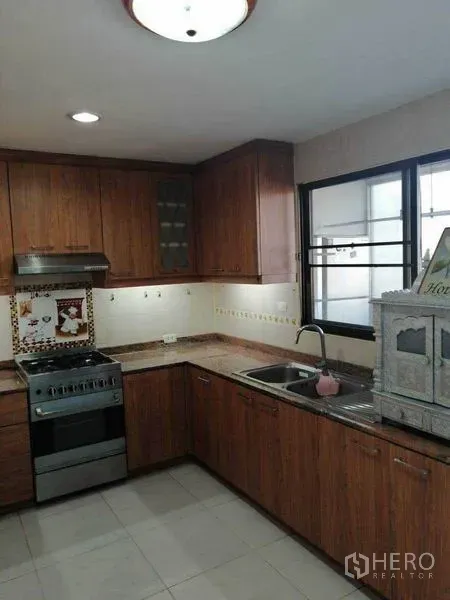 Condominium for rent in Watthana, Bangkok - U-shaped kitchen with wooden cabinetry, gas stove, range hood and a window.