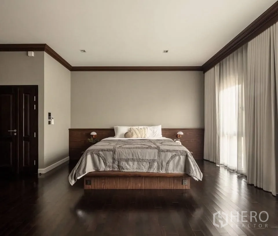 Detached House for rent or sale in Lat Krabang, Bangkok - Minimal master bedroom with king bed, dark wood flooring, and tall curtains.