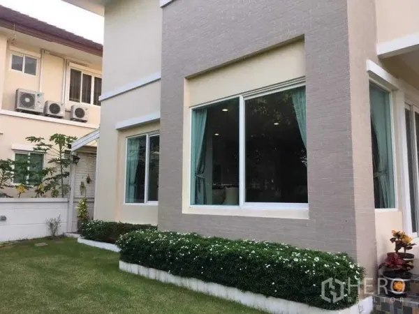 独立式住宅 出售在Bang Kruai, Nonthaburi - 一楼转角大窗配窗帘，旁有精致小花园。