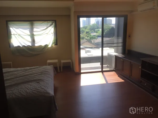 Townhouse for rent in Khlong Toei, Bangkok - Bedroom with built-in cabinetry and balcony access, with city views in the distance.