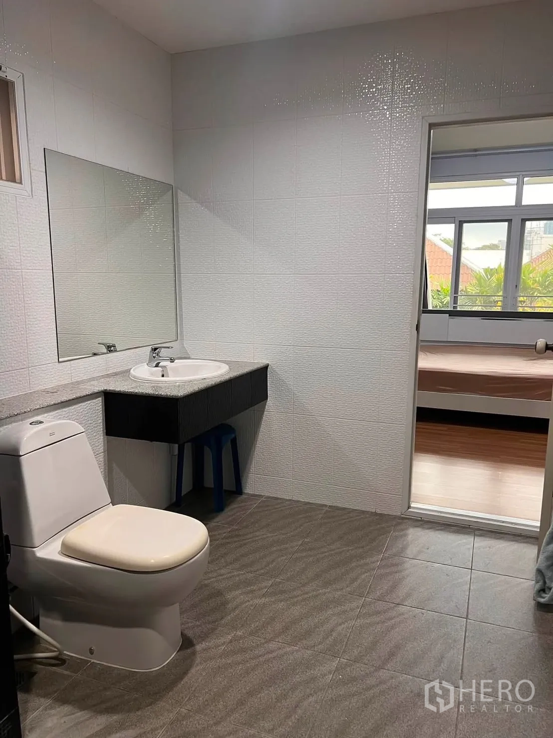 Detached House for rent in Watthana, Bangkok - Bathroom with toilet, basin, large mirror, and a doorway to the adjacent bedroom.